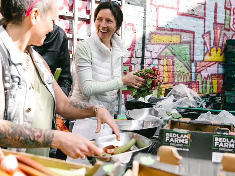 Weighing produce into a bowl at the Vegbox packing yard, in front of a colourful mural
