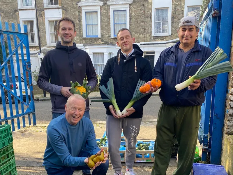 Four volunteers at the packing yard gate holding leeks, pears and a squash